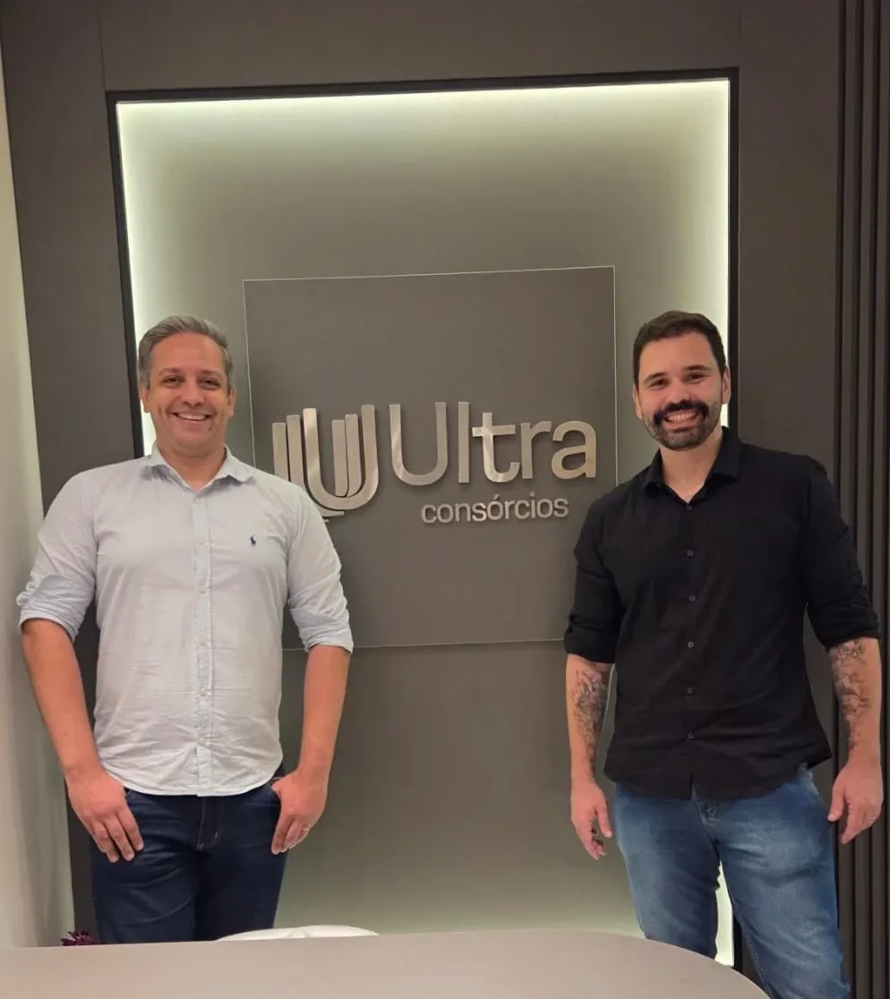 Sócios da Ultra Consórcios no escritório, diante do logo da empresa